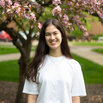 grace in a white tee smiling in front of a pink flowering tree